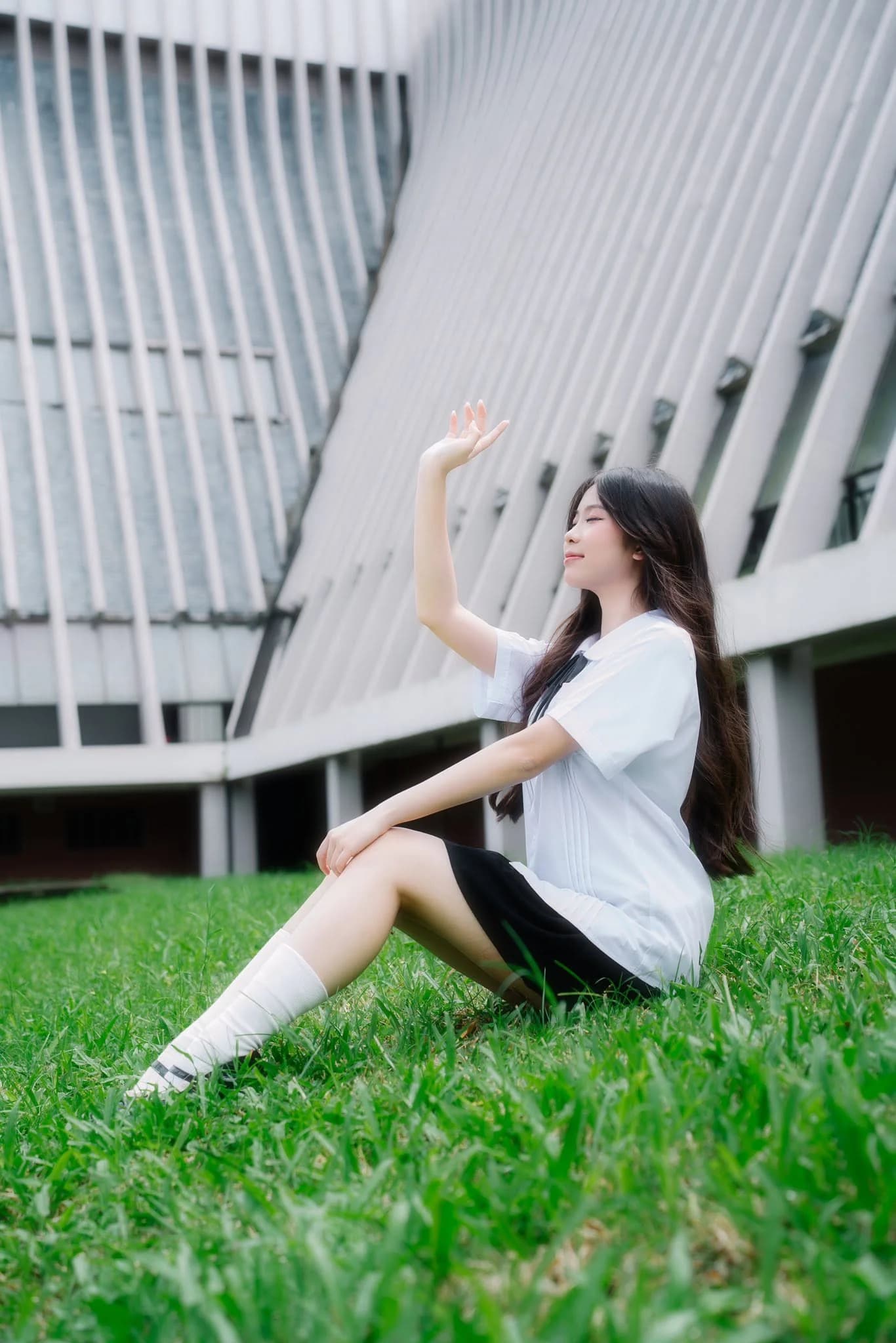 Bạn nữ ngồi trên bãi cỏ trong trang phục thanh xuân